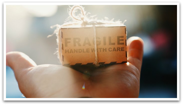 Hand holding a box reading "Fragile handle with care" wrapped in twine with a bow.
