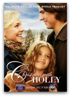 Poster of a couple smiling at each other wearing winter clothes. Snow dusted Christmas trees are in the background and a young girl with messy hair in the foreground. Text reads "Christmas with Holly".