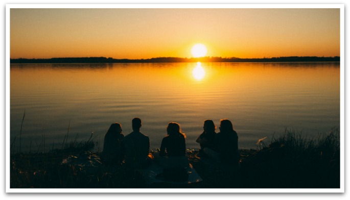 group sitting by a large lake watching the sunset