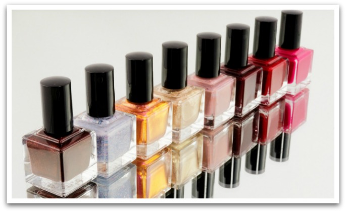 A row of square shaped sparkly nail polishes reflecting on a mirror base.