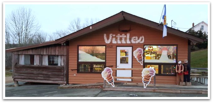 Vittles Family Restaurant New Ross exterior. Ice cream posters and a Nova Scotia flag are displayed on the brown building with "Vittles" painted above the white door.